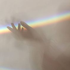 a person's hand reaching up into the sky with a rainbow in the background