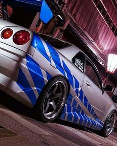 a white car with blue stripes painted on it's hood parked in front of a building