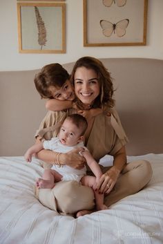 a woman sitting on top of a bed holding a baby next to her and smiling at the camera