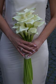 a woman in a white dress holding a bouquet of calla lilies on her wedding day