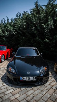 two cars parked next to each other in front of some trees and bushes on a brick road