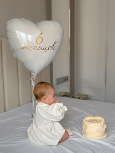 a baby sitting on a bed next to a cake and balloon that says 6 mesofy