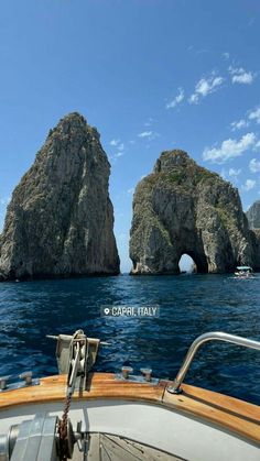 two large rock formations in the ocean with a boat passing by them and another one sitting on the side of the boat