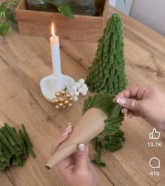 someone is decorating a small christmas tree with green leaves and gold decorations on the table