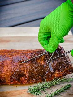 a person in green gloves cutting up a large piece of meat on a wooden board