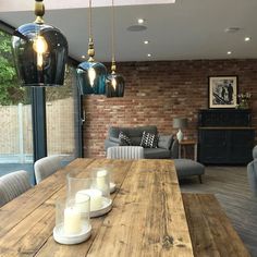 a wooden table with candles on it in front of a brick wall and large windows