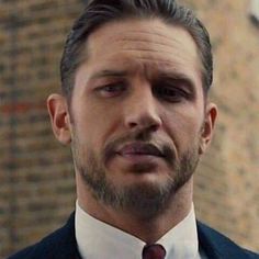 a man wearing a suit and tie in front of a brick building with his eyes closed