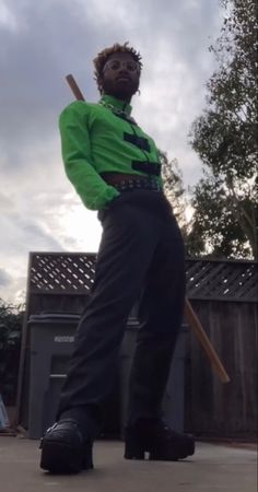 a man in green shirt and black pants holding a baseball bat