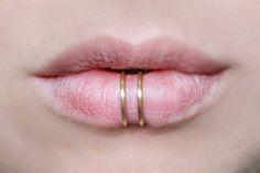 a woman's lips with two gold rings on her lip and one pink lipstick