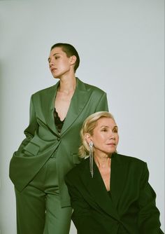 two women in green suits sitting next to each other and one woman is wearing earrings