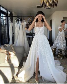 a woman standing in front of a mirror wearing a white wedding dress with high slit