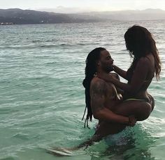 a man and woman in the water with no shirt on, one is sitting on his back