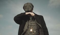 a man in a suit and hat holding his hand to his face while standing under a cloudy blue sky