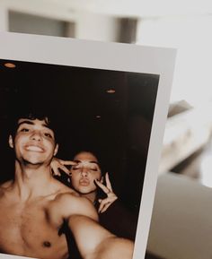 a man holding up a polaroid photo with his shirt off and two women behind him