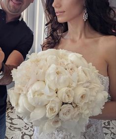 a man holding a bouquet of white flowers next to a woman in a wedding dress