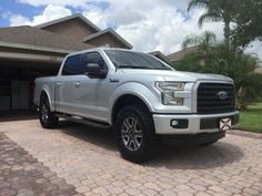 a silver truck is parked in front of a house with brick driveway and palm trees