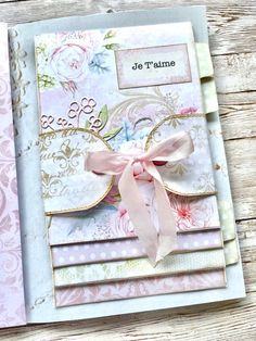 a close up of a card on a wooden surface with flowers and ribbons attached to it