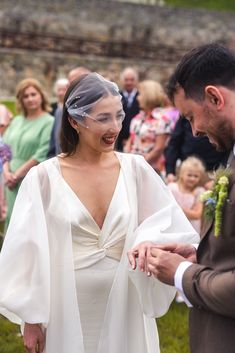 a woman in a wedding dress and veil smiles as she holds the groom's hand