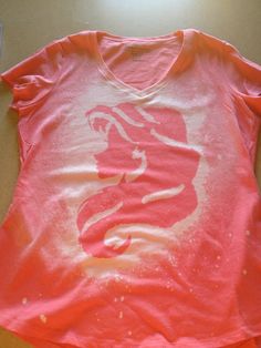 a pink shirt with white paint on it sitting on top of a wooden table next to a cell phone