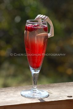 a glass filled with liquid sitting on top of a wooden table next to a forest