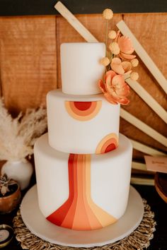 a three tiered white cake with orange and red designs on the top, sitting on a table