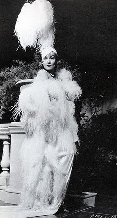 an old photo of a woman in a feathered dress and headdress standing on steps