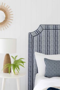 a bedroom with white walls and blue plaid headboard on the bed, next to a plant