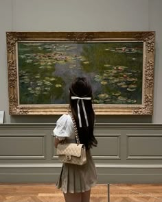 a woman standing in front of a painting holding a white bag and looking at it