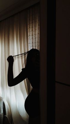 a woman standing in front of a window next to a white curtain with her arm up