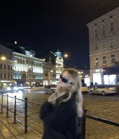 a woman with sunglasses on walking down the street in front of some buildings at night