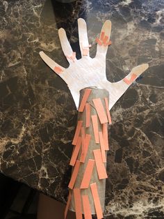 a hand made out of construction paper on top of a marble table with orange strips