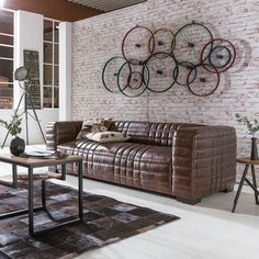 a brown leather couch sitting in front of a wall mounted bike wheel art on a brick wall