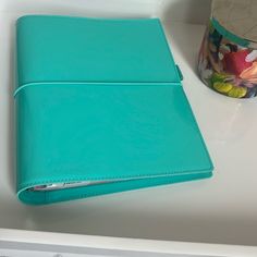 a blue leather notebook sitting on top of a white counter next to a cup and vase