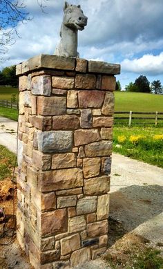 a statue of a dog on top of a stone pillar in front of a field