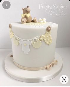 a white cake with a teddy bear on top and baby clothes hanging from it's sides