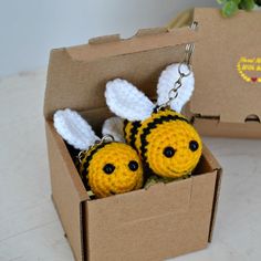 two crocheted bee keychains are in a cardboard box on a table