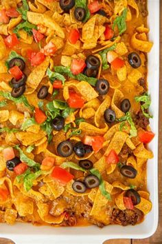 a casserole dish with tortilla chips, black olives and tomatoes