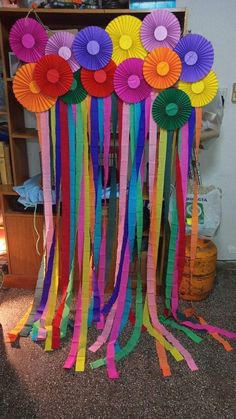 some colorful paper flowers and streamers are hanging from the ceiling in front of a bookshelf