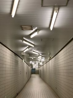 a long hallway with white tile walls and ceiling lights