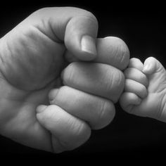 a black and white photo of a baby's hand holding the finger of an adult