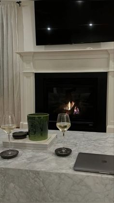 two glasses of wine are sitting on a table in front of a fireplace with a flat screen tv above it