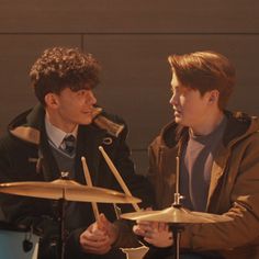 two young men sitting next to each other with drums