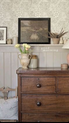 a dresser with flowers and vases on it in front of a wallpapered background