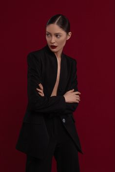 a woman with her arms crossed standing in front of a red background wearing a black suit