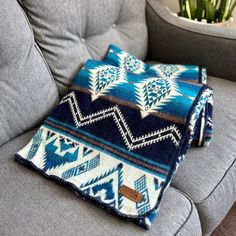 a blue and white blanket sitting on top of a gray couch next to a potted plant