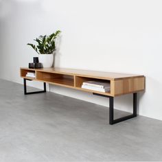 a wooden table with a plant on it in front of a white wall and concrete floor