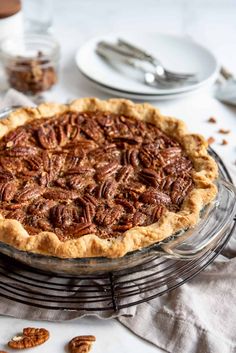 a pecan pie sitting on top of a metal rack next to plates and utensils