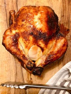 a whole chicken sitting on top of a wooden cutting board next to a knife and fork