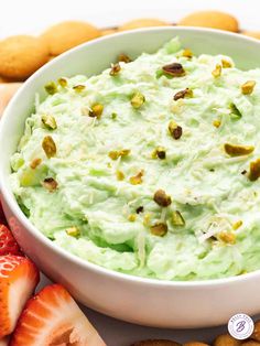 a white bowl filled with whipped cream surrounded by sliced strawberries and pistachios