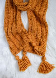 an orange knitted scarf with tassels laying on a white furnishing